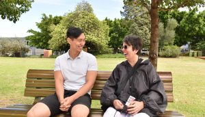 a man and a woman sitting on a part bench smiling at each other. The woman is laughing.