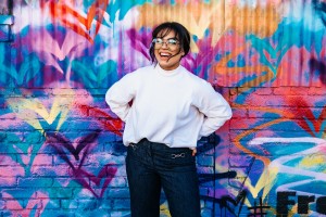 Young person smiling in front of graffitied wall