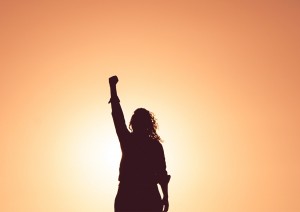 Silhouette of woman with fist in the air surrounded by sunshine